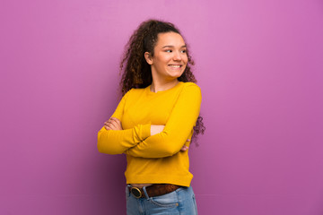 Teenager girl over purple wall with arms crossed and happy