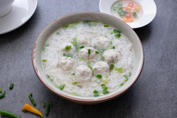 Rice soup with chicken ball and scallion in gray bowl on table.