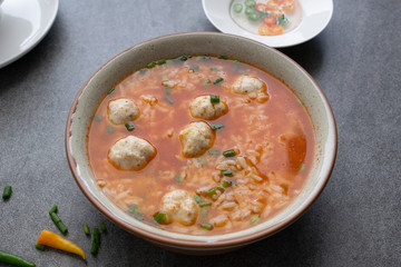 Rice spicy soup with chicken ball and chilli in gray bowl on table.