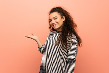 Teenager girl over pink wall holding copyspace imaginary on the palm to insert an ad