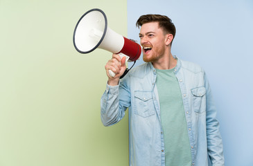 Redhead man over colorful background shouting through a megaphone