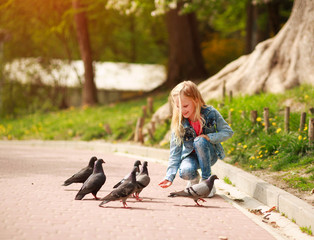 Friendly joyful girl child feeds pigeons in city summer park