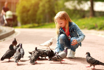 Friendly joyful girl child feeds pigeons in city summer park