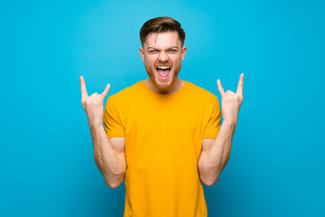 Redhead man over blue wall making rock gesture