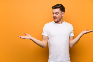 Redhead man over brown wall holding copyspace with two hands