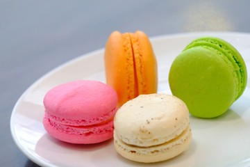 In senlective focus a group of macaroons,famous French dessert in a white plate with wooden dinning table 