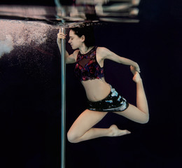 Obraz premium Young, fit, slim woman with pole underwater in the swimming pool on black background