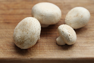white champignon mushrooms lie on a wooden board