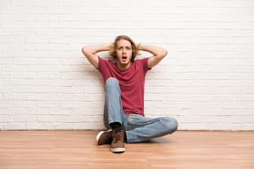 Blonde man sitting on the floor frustrated and takes hands on head © luismolinero