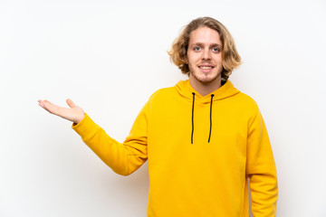 Blonde man with  sweatshirt over white wall holding copyspace imaginary on the palm to insert an ad