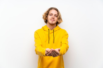 Blonde man with  sweatshirt over white wall holding copyspace imaginary on the palm to insert an ad