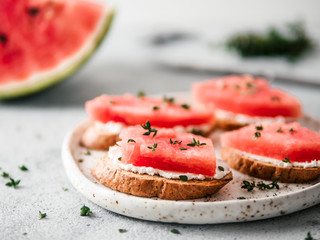 Toasts with soft cheese, watermelon and fresh thyme.Salty cheese,sweet watermelon and spicy thyme on crispy grilled bread slices. Idea and recipe for unusual healthy breakfast, summer snack or lunch