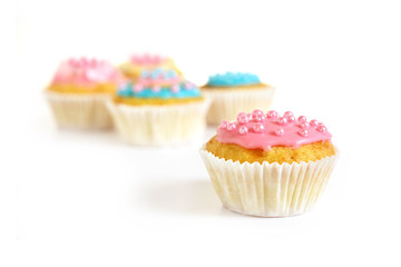 muffin or cupcake with pink icing and sugar pearls, more cupcakes blurry in the background,...