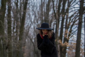 The girl in a black coat, a shovel hat and with red lipstick on lips, walks in the park. Style and modern fashion.