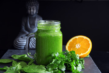 Grüner Smoothie mit Buddha Statue im Hintergrund
