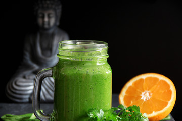 Grüner Smoothie mit Buddha Statue im Hintergrund