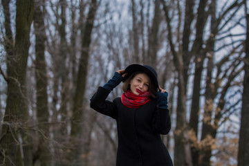 The girl in a black coat, a shovel hat and with red lipstick on lips, walks in the park. Style and modern fashion.