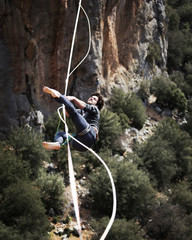 A man is walking along a stretched sling. Highline in the mountains. Man catches balance....