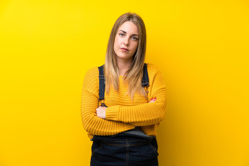 Fototapeta premium Woman with overalls over isolated yellow wall keeping arms crossed
