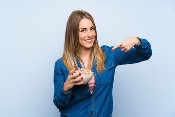 Happy young woman with bowl of cereals over isolated blue wall