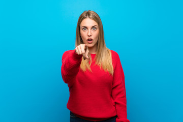 Woman with red sweater over blue wall surprised and pointing front