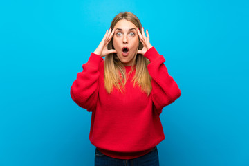 Woman with red sweater over blue wall with surprise expression