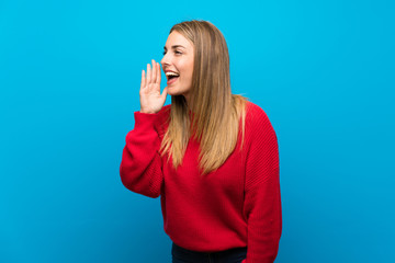 Woman with red sweater over blue wall shouting with mouth wide open to the lateral