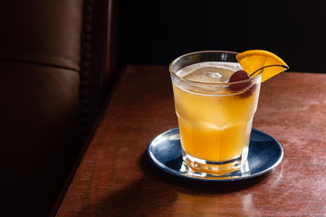 Amaretto Sour Cocktail on the Rocks with a Cherry and Orange Garnish in a Dark Luxurious Bar
