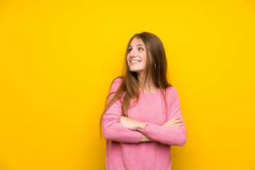 Obraz premium Young woman with long hair over isolated yellow wall looking up while smiling