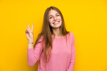 Young woman with long hair over isolated yellow wall smiling and showing victory sign