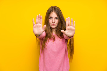 Young woman with long hair over isolated yellow wall making stop gesture and disappointed