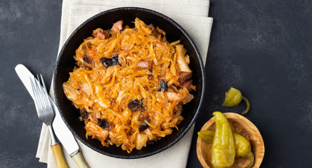 Traditional dish of polish cuisine - Bigos from fresh cabbage, meat and prunes. Top view. Dark background.