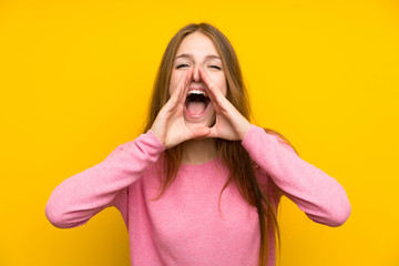 Young woman with long hair over isolated yellow wall shouting and announcing something