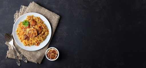 Traditional asian dish - pilaf from from rice, vegetables and meat in a plate on black background. Top view. Long format.