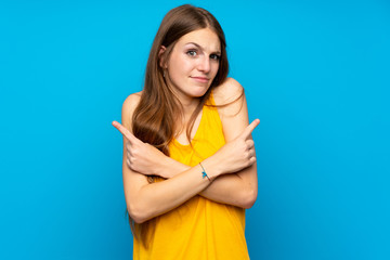 Young woman with long hair over isolated blue wall pointing to the laterals having doubts