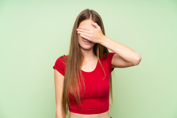 Young woman with long hair over isolated green wall covering eyes by hands