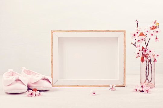 Mock up with empty picture frame, pink tender spring flowers and small baby girl shoes