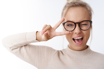 Hey smile you. Portrait of cheeky and cute glamour blond woman in glasses combed hair and sweater winking happily showing peace victory gesture as fooling around, being optimistic - obrazy, fototapety, plakaty