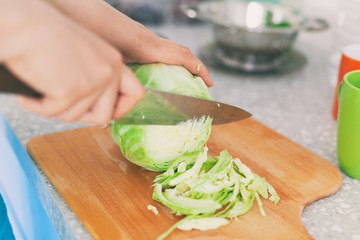Person cuts cabbage on cutting board in kitchen
