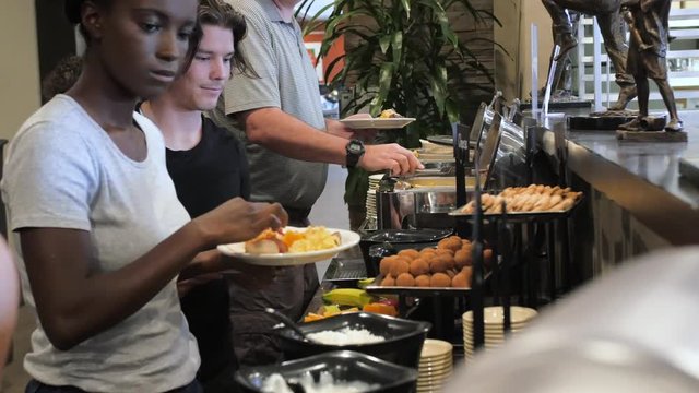 mixed racial husband wife in breakfast buffet line. A mixed racial couple and baby daughter make their way down a hot hotel breakfast buffet line and dish up their food.