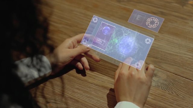Unrecognizable woman working on a futuristic tablet with a hologram text E-ticket. Women's hands with future holographic technology at a wooden table