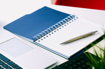 Closeup of white desktop with laptop, coffee cup, notepads, pen, calculator and other items.