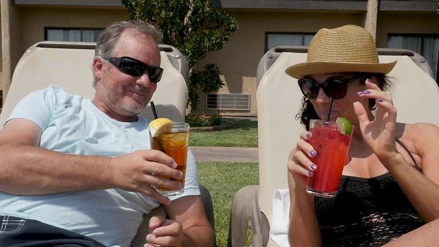 poolside service couple clink glasses. This couple touch drink glasses as they enjoy drinks lounging next to a hotel pool.