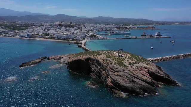 Aerial drone panoramic view video of iconic and unique Temple of Apollon or Portara (Gate) with breathtaking views to port - town and castle of Naxos island and the Aegean blue sea, Cyclades, Greece