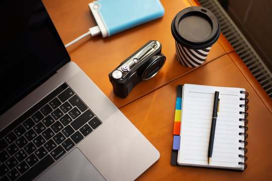 Work wooden desk of photographer with camera near cup of coffee, laptop, external hdd drive and empty notebook