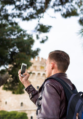 Handsome man, tourist, with backpack taking pictures on a smartphone the White Tower in the center Thessaloniki, Greece