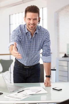 Businessman at office desk offering hand