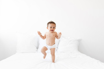 Happy toddler in diaper dancing on bed