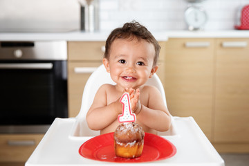 Happy baby in high chair with cake celebrating first birthday