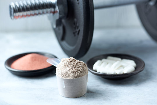 Scoop of Whey Protein, Beta-alanine capsules, Creatine Powder and a dumbbell in background. Sport nutrition. Stone / Wooden background. Copy space